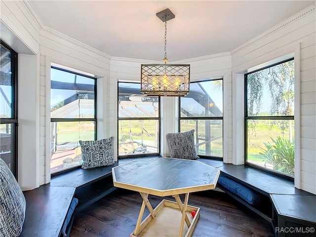 dining area featuring dark wood-style floors, a sunroom, ornamental molding, and wooden walls