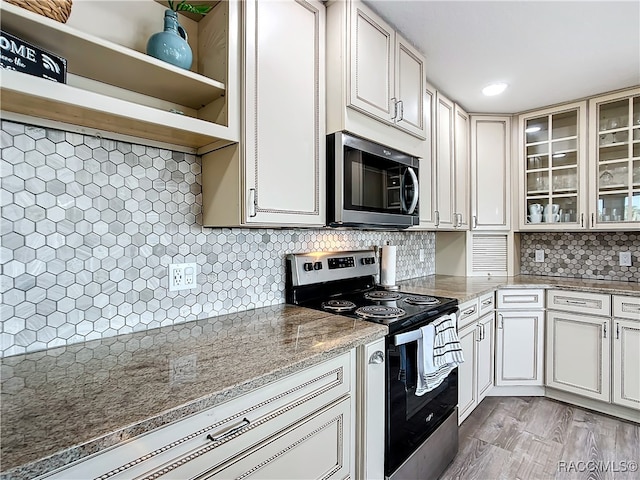 kitchen featuring tasteful backsplash, stainless steel microwave, glass insert cabinets, light stone countertops, and range with electric cooktop