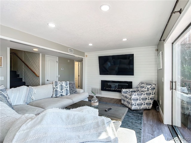 living room featuring dark wood-type flooring, a large fireplace, wood walls, and a textured ceiling