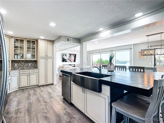 kitchen with a sink, cream cabinetry, light wood finished floors, glass insert cabinets, and pendant lighting