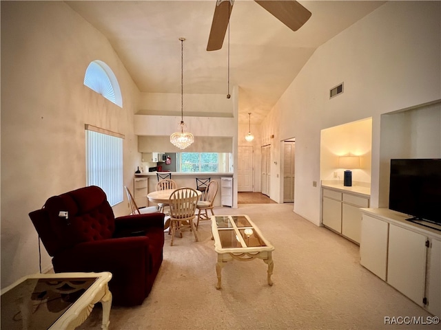 carpeted living room with high vaulted ceiling and ceiling fan with notable chandelier