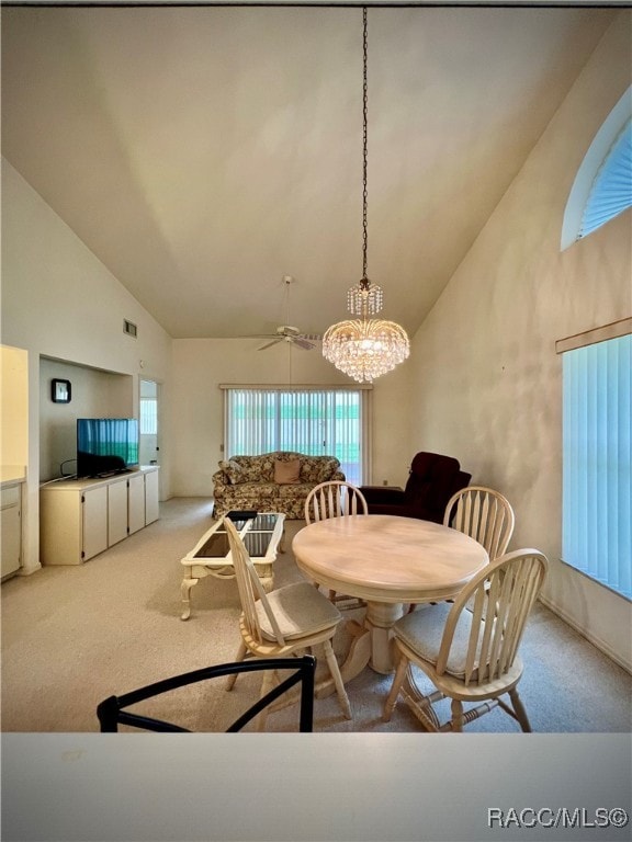 carpeted dining space featuring ceiling fan with notable chandelier and high vaulted ceiling