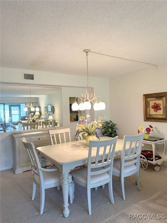 carpeted dining area featuring a textured ceiling and an inviting chandelier