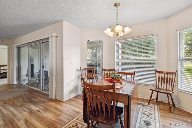 dining area with light hardwood / wood-style floors, a textured ceiling, and a chandelier