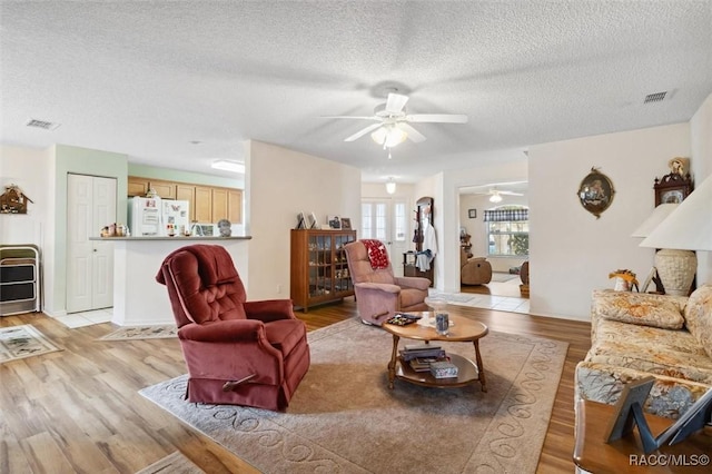 living room featuring ceiling fan, a textured ceiling, and light hardwood / wood-style flooring