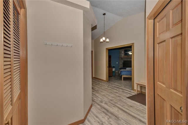 corridor featuring an inviting chandelier, light hardwood / wood-style floors, and vaulted ceiling