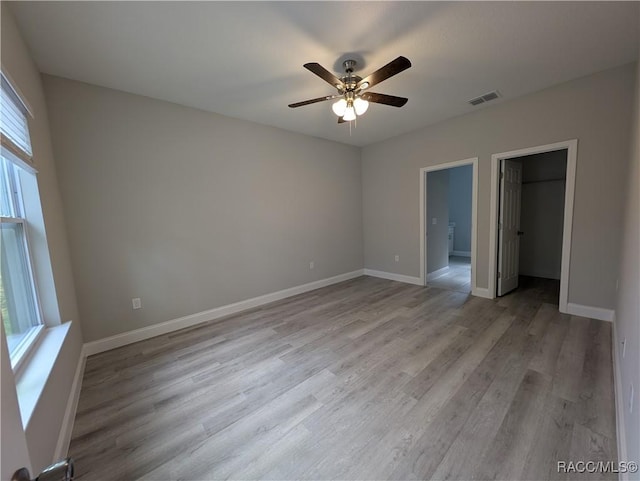 unfurnished bedroom featuring light hardwood / wood-style flooring, ceiling fan, connected bathroom, a walk in closet, and a closet