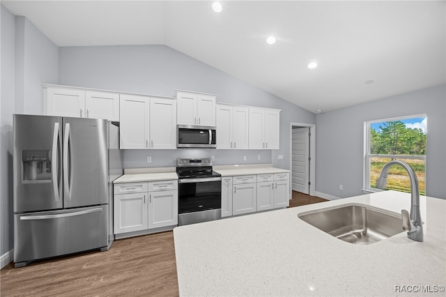 kitchen featuring white cabinets, stainless steel appliances, vaulted ceiling, and sink