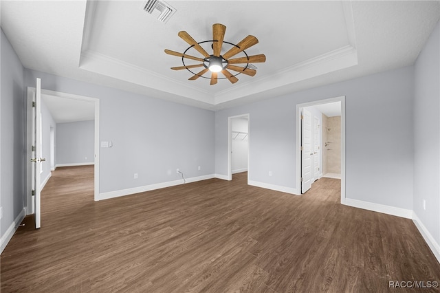 unfurnished bedroom with a walk in closet, crown molding, ceiling fan, dark hardwood / wood-style floors, and a tray ceiling