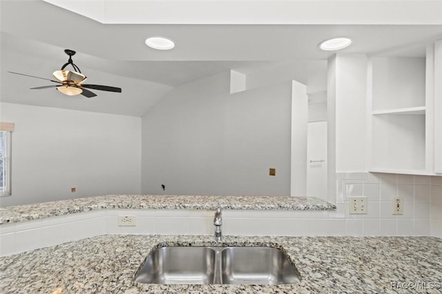 kitchen featuring light stone counters, vaulted ceiling, sink, and tasteful backsplash