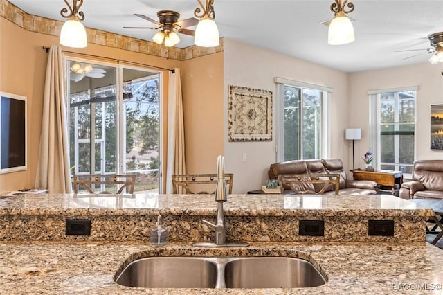 kitchen featuring ceiling fan, a sink, open floor plan, light stone countertops, and pendant lighting