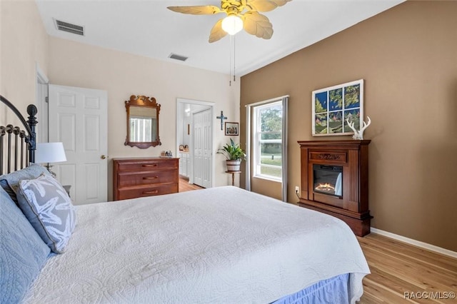 bedroom featuring light wood-type flooring, a glass covered fireplace, visible vents, and baseboards