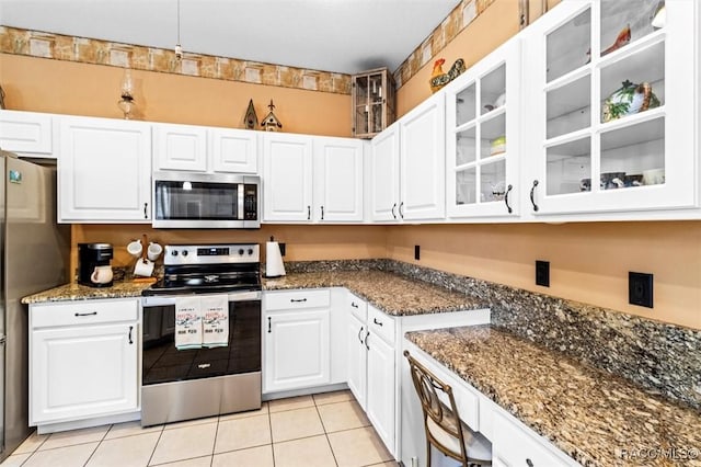 kitchen with white cabinets, dark stone counters, glass insert cabinets, stainless steel appliances, and light tile patterned flooring