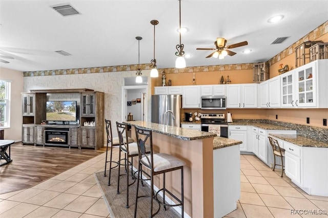 kitchen with glass insert cabinets, stainless steel appliances, white cabinets, dark stone counters, and a center island with sink