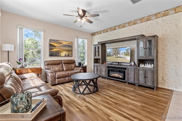 living room with ceiling fan, a glass covered fireplace, wood finished floors, and baseboards