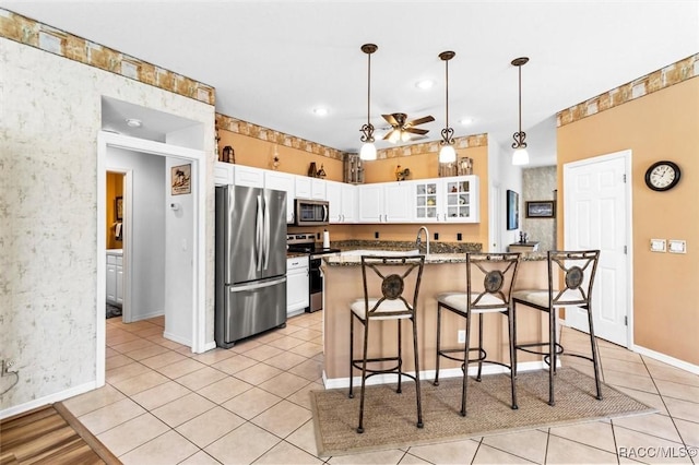 kitchen featuring glass insert cabinets, white cabinets, appliances with stainless steel finishes, a center island with sink, and decorative light fixtures