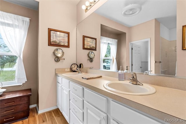 full bath featuring wood finished floors, a sink, a shower stall, and double vanity