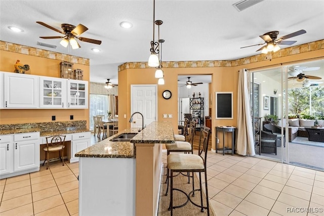 kitchen with a sink, white cabinetry, dark stone countertops, glass insert cabinets, and pendant lighting