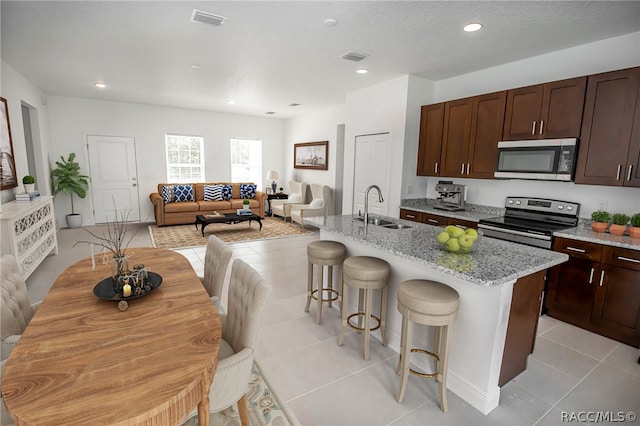 kitchen with sink, a kitchen breakfast bar, a kitchen island with sink, light tile patterned floors, and appliances with stainless steel finishes