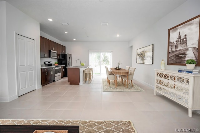 kitchen with a center island with sink, sink, light tile patterned floors, dark brown cabinetry, and stainless steel appliances