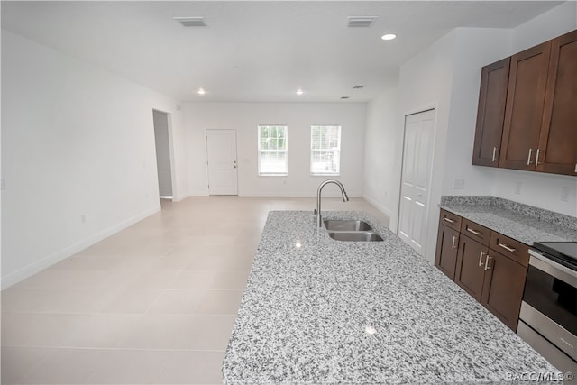 kitchen with stainless steel electric range, light stone counters, dark brown cabinets, and sink