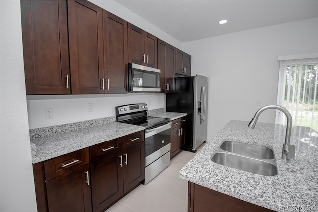 kitchen with dark brown cabinets, stainless steel appliances, light stone counters, and sink