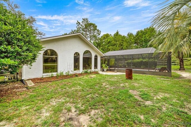 4357 N Indianhead Rd, Hernando, FL 34442 - rear view of house featuring stucco siding, a lawn, glass enclosure, and a carport