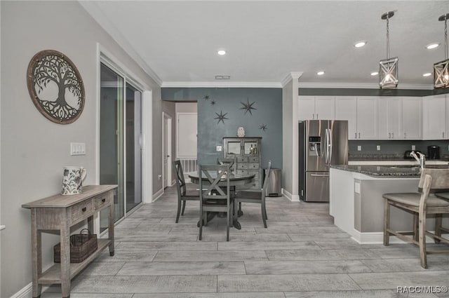 kitchen with a breakfast bar, stainless steel fridge with ice dispenser, pendant lighting, dark stone counters, and white cabinets