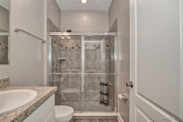 bathroom featuring vanity, a shower with door, and toilet