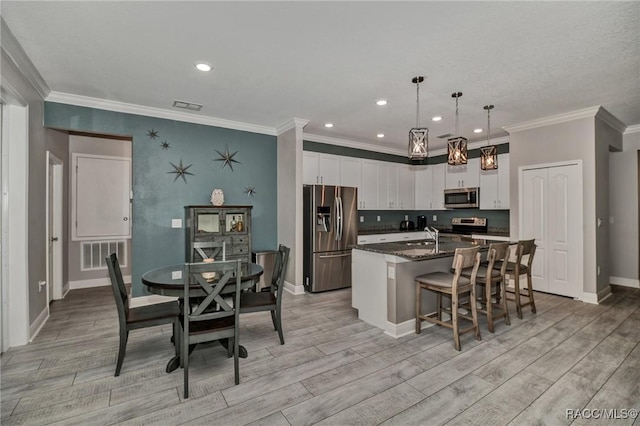 kitchen with white cabinetry, dark stone countertops, hanging light fixtures, stainless steel appliances, and a center island with sink