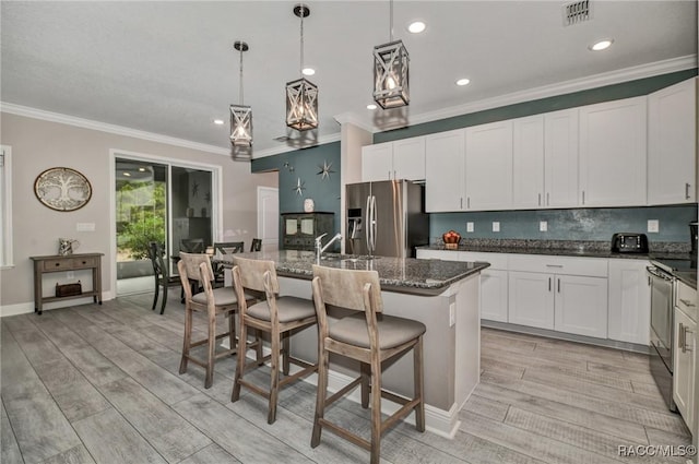 kitchen with white cabinetry, a kitchen bar, dark stone counters, stainless steel appliances, and a center island with sink