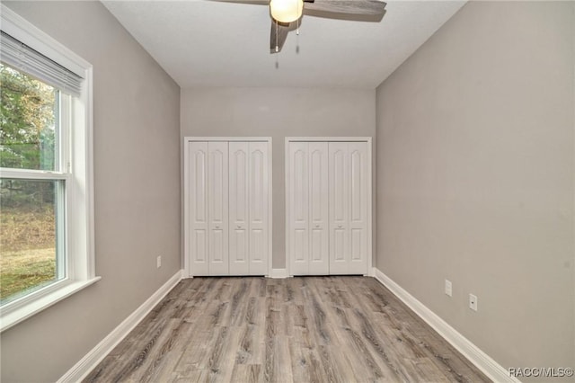 unfurnished bedroom with multiple closets, ceiling fan, light hardwood / wood-style floors, and multiple windows