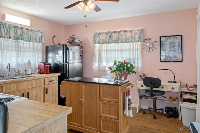 kitchen featuring black fridge, sink, ceiling fan, light wood-type flooring, and a textured ceiling