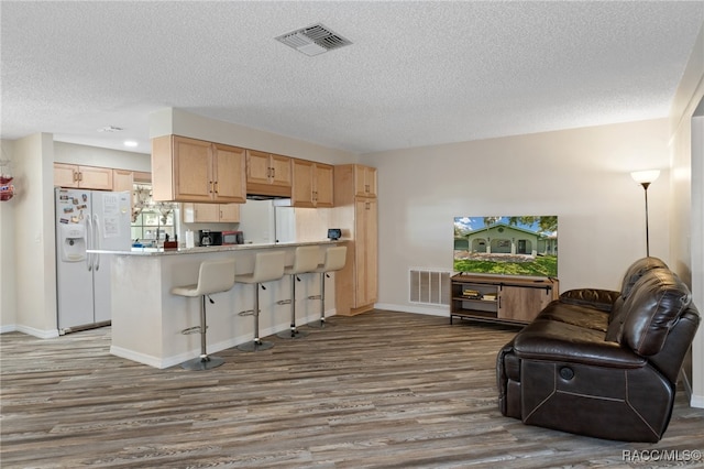 kitchen featuring a breakfast bar area, light brown cabinetry, hardwood / wood-style floors, and white refrigerator with ice dispenser