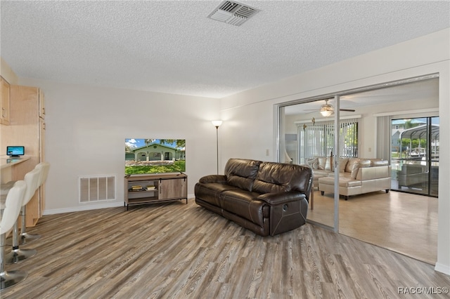 living room featuring wood-type flooring, a textured ceiling, and ceiling fan