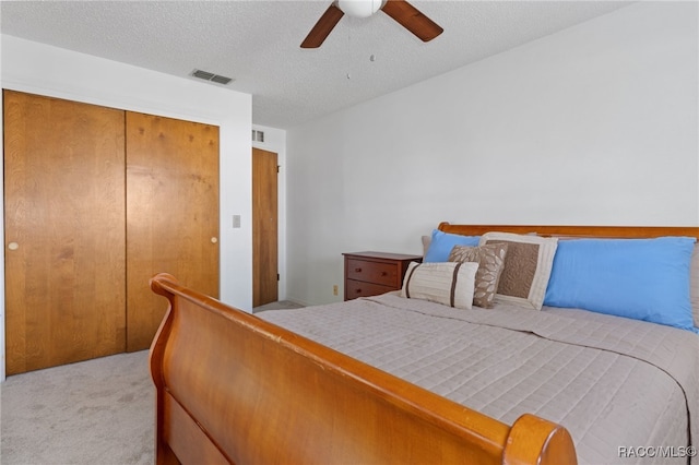 bedroom featuring ceiling fan, a closet, light colored carpet, and a textured ceiling