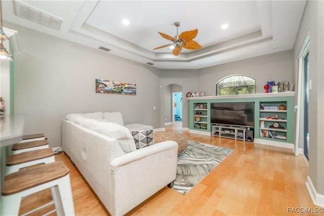 living room with a raised ceiling, ceiling fan, and wood-type flooring