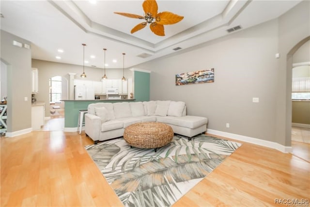 living room featuring ceiling fan, light hardwood / wood-style floors, and a tray ceiling