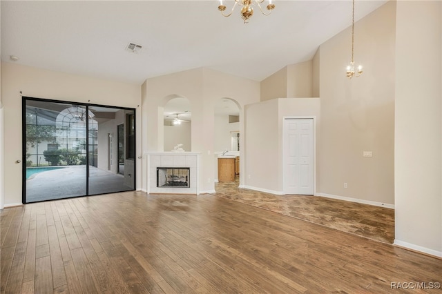 unfurnished living room featuring wood finished floors, visible vents, a tiled fireplace, and an inviting chandelier