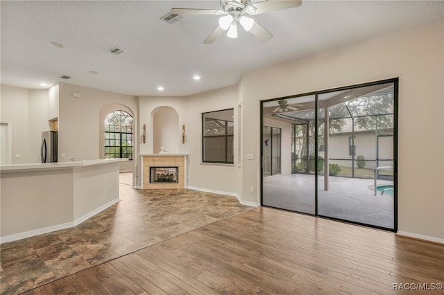 unfurnished living room with a ceiling fan, a tile fireplace, visible vents, and wood finished floors