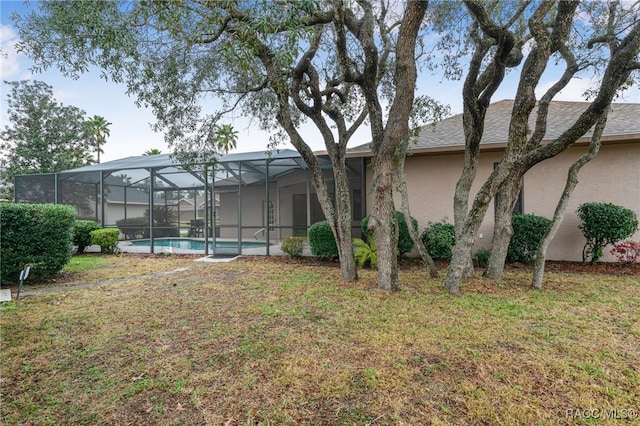 rear view of property featuring a yard, an outdoor pool, a lanai, and stucco siding