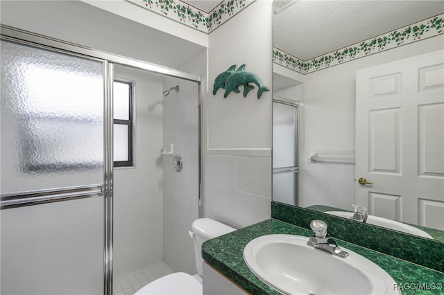 full bathroom featuring tile walls, toilet, vanity, a shower stall, and a textured ceiling