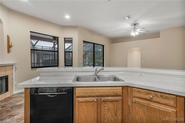 kitchen featuring tile counters, visible vents, a tiled fireplace, a sink, and dishwasher