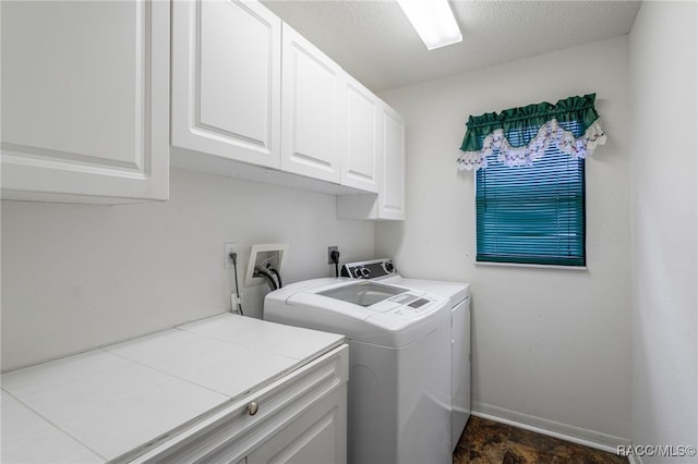 laundry area featuring cabinet space, baseboards, a textured ceiling, and washing machine and clothes dryer