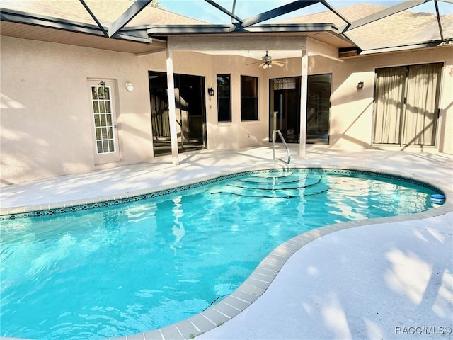 outdoor pool featuring glass enclosure, a patio area, and a ceiling fan