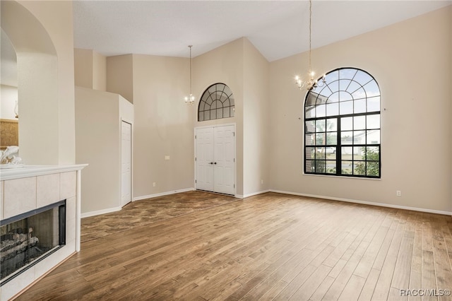 unfurnished living room with baseboards, a tile fireplace, wood finished floors, high vaulted ceiling, and a notable chandelier