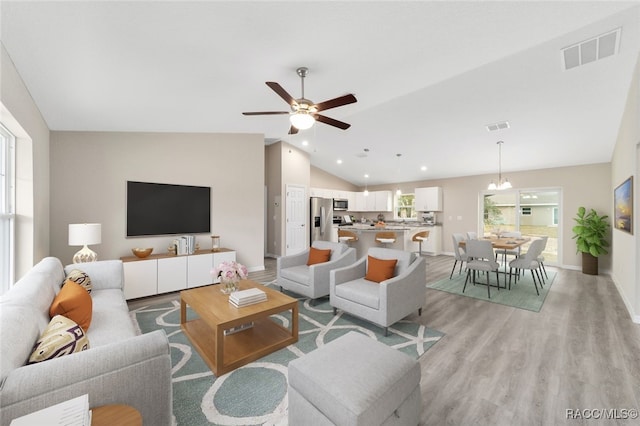 living room featuring ceiling fan with notable chandelier, light hardwood / wood-style floors, and lofted ceiling