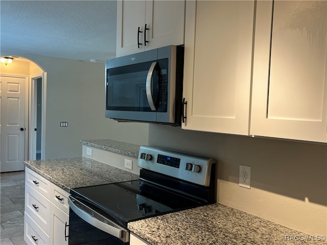 kitchen with a textured ceiling, stainless steel appliances, white cabinetry, and light stone counters