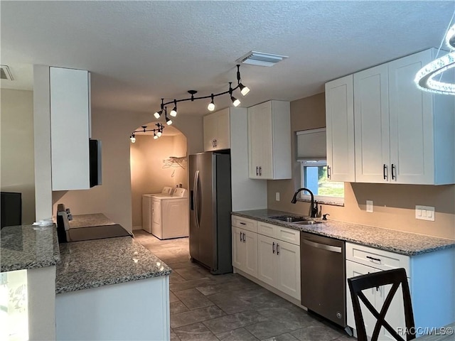 kitchen with light stone counters, stainless steel appliances, washer and clothes dryer, sink, and white cabinets