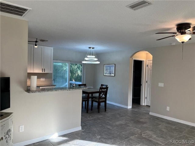 kitchen featuring kitchen peninsula, ceiling fan, decorative light fixtures, stone counters, and white cabinetry